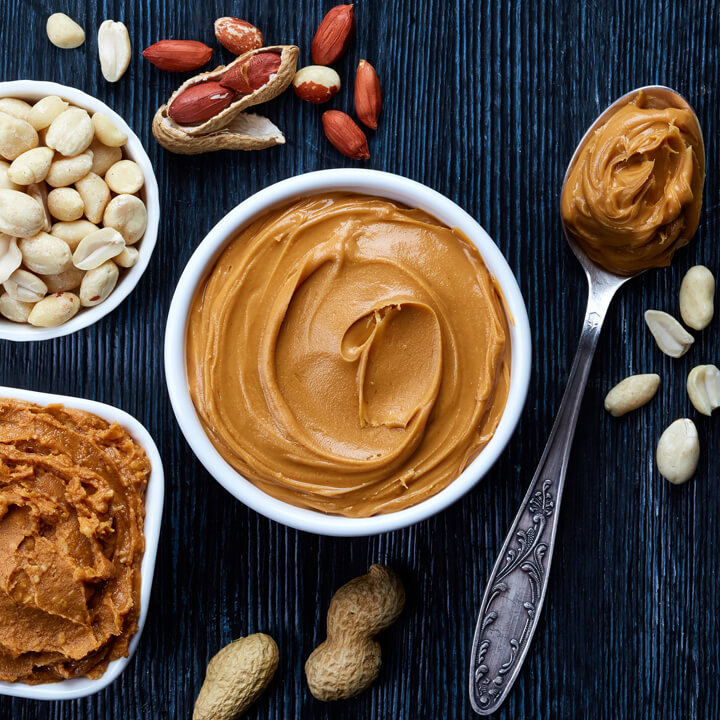 Two bowls of peanut butter and peanuts on dark wooden background