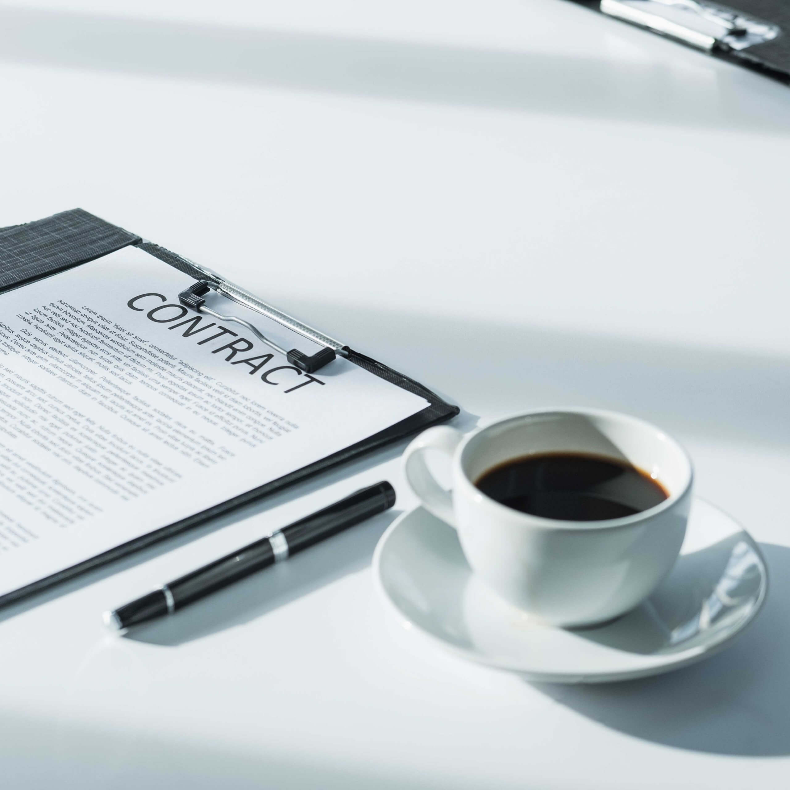 An image of a contract, pen and coffee on a table, A visual metaphor for the topic of this article the importance of IP indemnities in sponsorship agreements